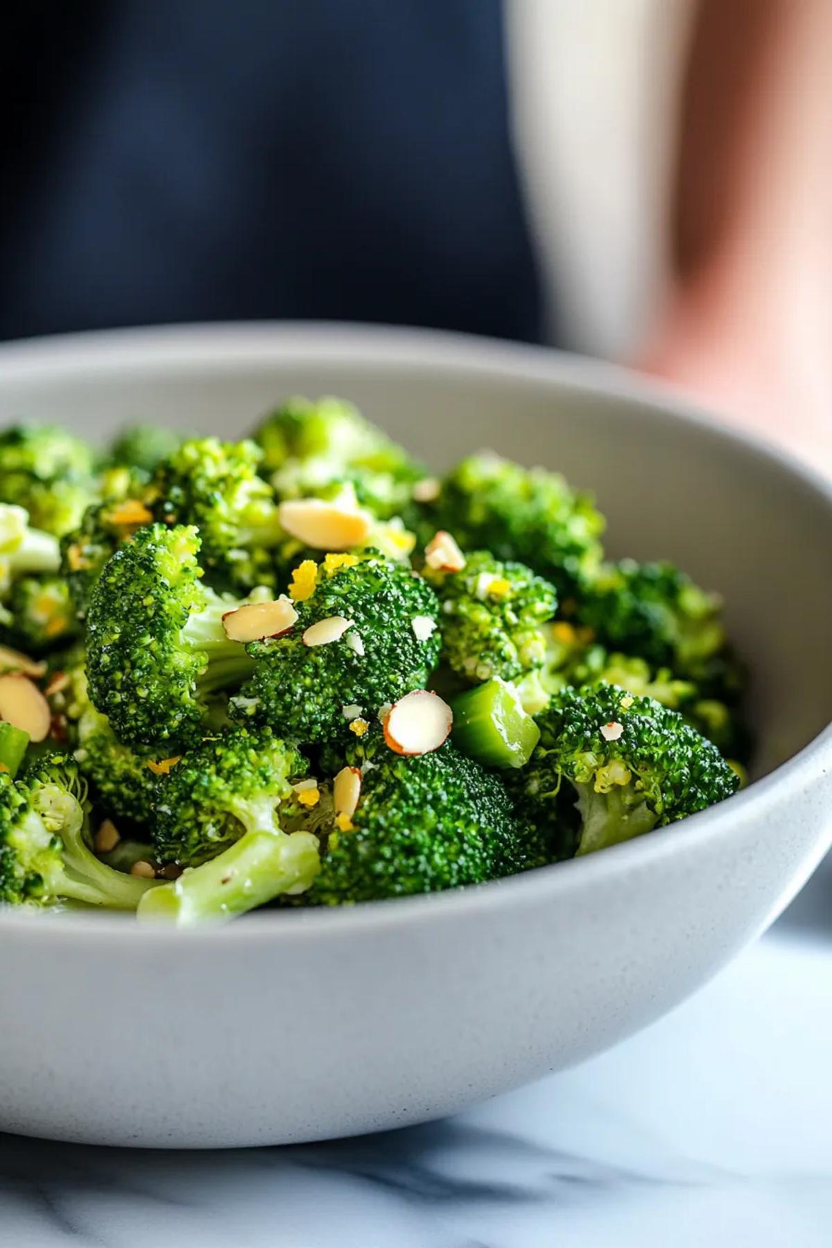 Steamed broccoli florets glistening with a citrus almond drizzle on a white platter. card